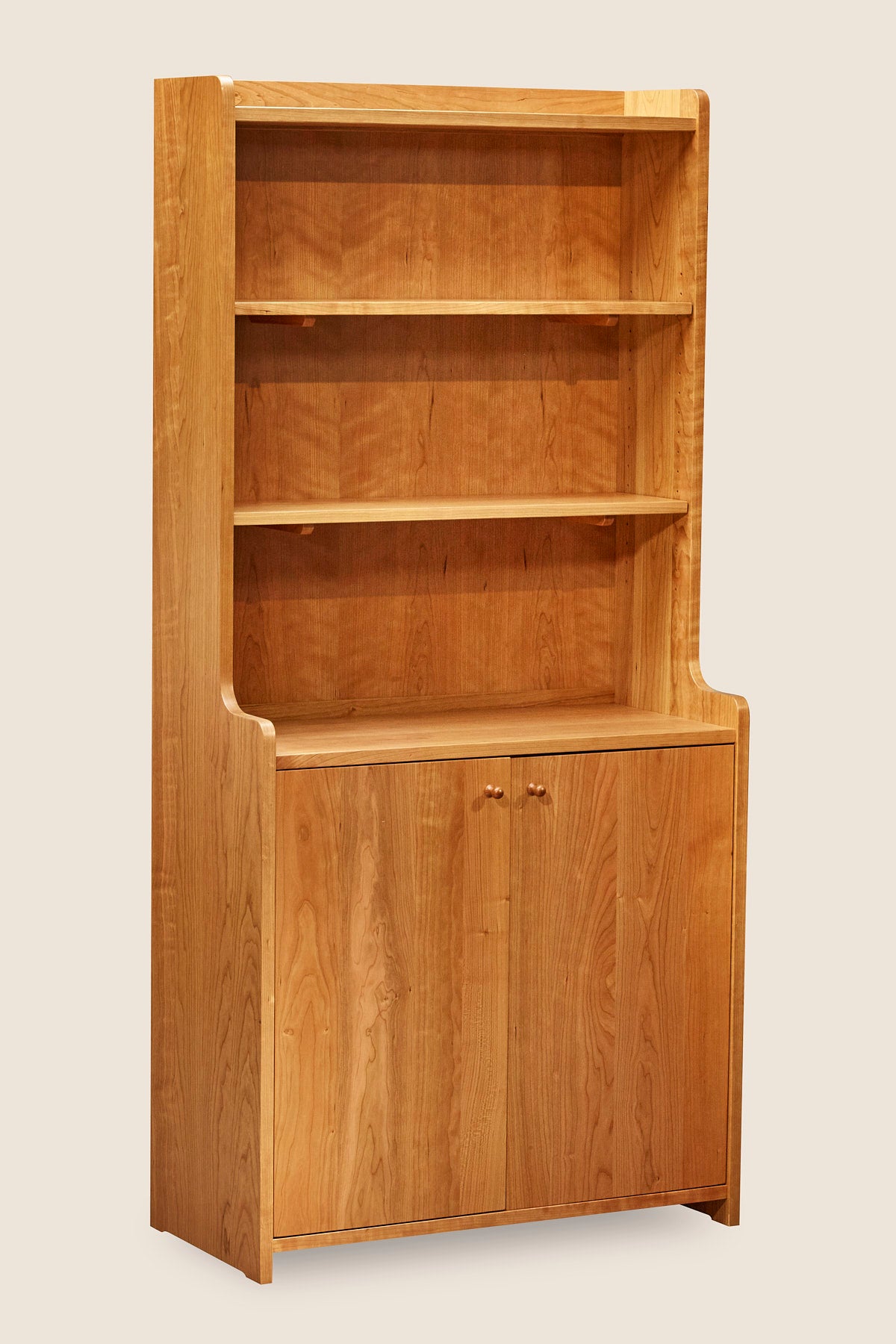 Tiered bookcase with rounded corners and doors over base, built in cherry. 